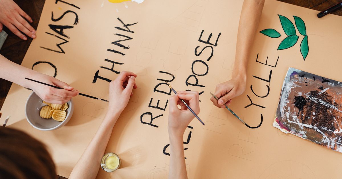 Group creating a poster on environmental themes with words like recycle, reuse, and reduce.